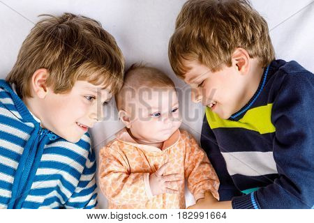 Two happy little preschool kids boys with newborn baby girl, cute sister. Siblings, twins children and baby playing together. Kids bonding. Family of three, love. kids in colorful fashion clothes