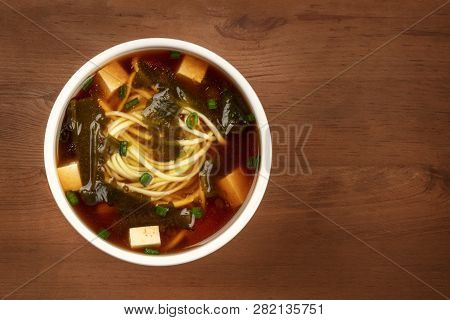 A Bowl Of Miso Shiru Soup With Tofu, Scallions, Noodles, And Wakame Seaweed, Shot From The Top On A 