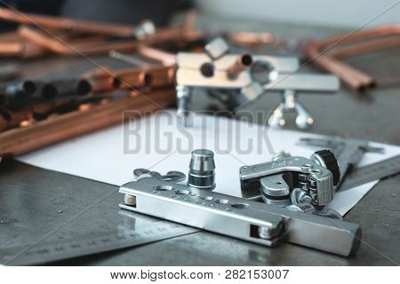 Brass Pipes, Pipe Rammer, Pipe Cutter Tool, Calipers, Pliers And A Blank Layout Drafts On A Fitter W