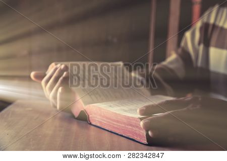A Man Sittding While Reading Bible Or Book In Room With Window Light