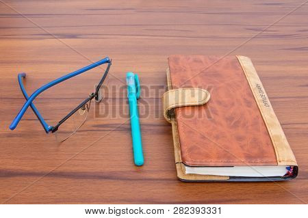 Brown Business Diary With Ball Pen And Specks Lying On Wooden Table