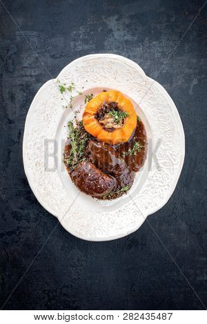 Traditional German braised pork cheeks in brown red wine sauce with mushroom and pumpkin as top view on a shabby chic design white plate with copy space 