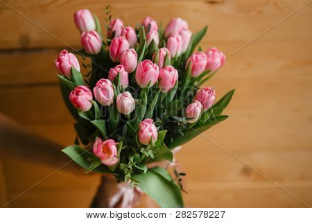 A Bouquet Of Pink Tulips In Womans Hands. Woden Background