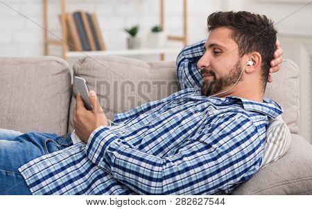 Man Watching Movie On Mobile Phone, Lying On Sofa, Relaxing At Home
