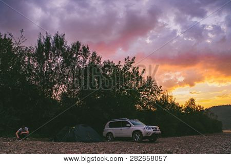 Camping At Rivershore On Sunrise. White Suv Car. Lifestyle