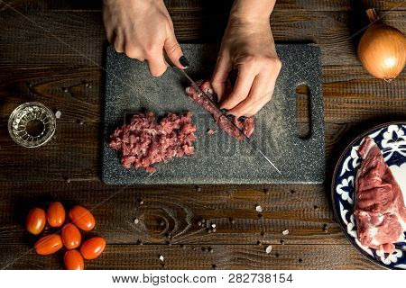 Cook Hands Cut Red Meat On The Board. Nearby Are Tomatoes, Onion, Butter