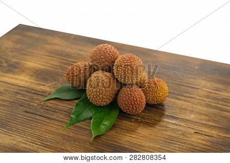Fresh Lychee And Peeled Showing The Red Skin And White Flesh With Green Leaf On A Wooden Background.