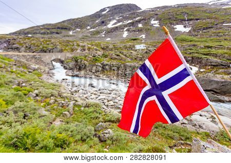Norwegian Flag Waving On Wind And Camper Car In Mountains In The Background. Travel, Holidays And Ad