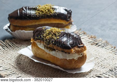 Eclairs With Pistachio And Black Chocolate And White Chocolate With Custard On Wooden Background And