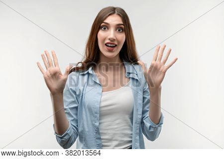Studio Shot Of Surprised Young Female With Long Chestnut Hair, Dressed In Casual Clothes, Smiling Ha
