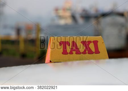 Taxi Light Sign Or Cab Sign In Drab Yellow Color With Red Text On The Car Roof At The Street Blurred