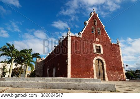 Red Colonial Church Itzimna In A Sunny Park With Palm Trees, Merida, Yucatan, Mexico