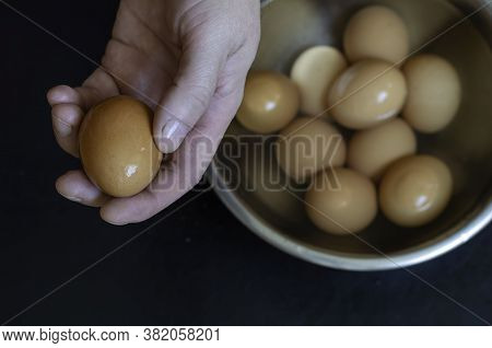 Male Hand Holds  Moist Brown Chicken Egg. Serve Boiled Eggs In Metal Bowl With Water Beside. Lunch P