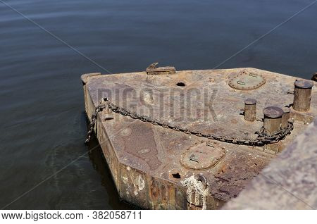 Old Rusty Metal Pontoon With Anchor Chain And Mooring Bollards. Holes In The Rotten Deck Of The Pont