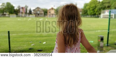 A Girl Sits With Her Back To The Camera And Watches A Football Match Of Childrens Teams. Beautiful L