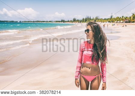 Puerto Rico beach bikini woman on summer vacation wearing pink rashguard for sun protection. Solar protective long sleeve shirt swimwear beachwear. Tropical lifestyle.