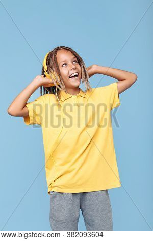 Joyful Little Boy With African Dreads Listening Music In Headphones Has Pleasant Smile Over Blue Bac