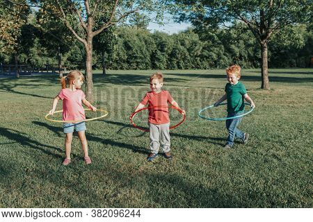 Cute Smiling Caucasian Preschool Girl Boys Friends Playing With Hoola Hoop In Park Outside. Kids Spo
