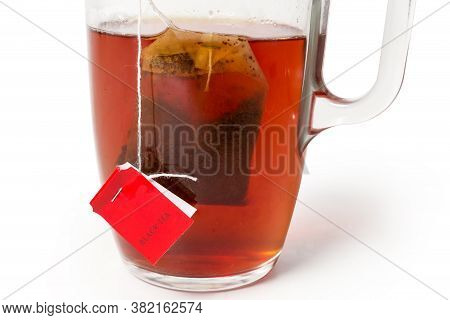 Bag Of Black Tea With Red Label In The Glass Cup With Freshly Brewed Tea On A White Background, Frag
