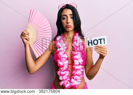 Beautiful hispanic woman wearing bikini and handfan holding hot word depressed and worry for distress, crying angry and afraid. sad expression. 