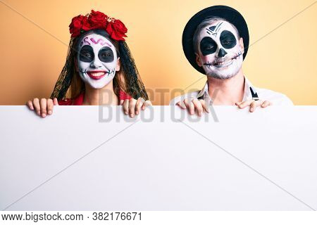 Couple wearing day of the dead costume holding blank empty banner looking positive and happy standing and smiling with a confident smile showing teeth 