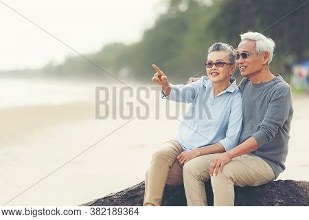Asian Lifestyle Senior Couple Hug And Pointing On The Beach Happy In Love Romantic And Relax Time.  