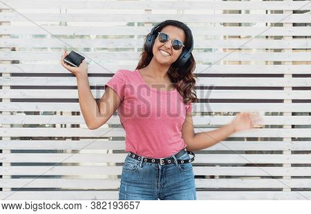 Young Women Listening Music With Headphones From Smartphone Near A Wall