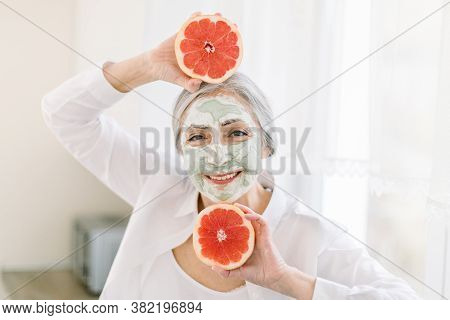 Close Up Beauty Portrait Of Pretty Elderly Grai Haired Woman With Mud Clay Facial Mask, Holding Near