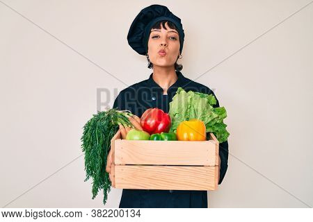 Beautiful brunettte woman chef holding fresh veggetables looking at the camera blowing a kiss being lovely and sexy. love expression. 
