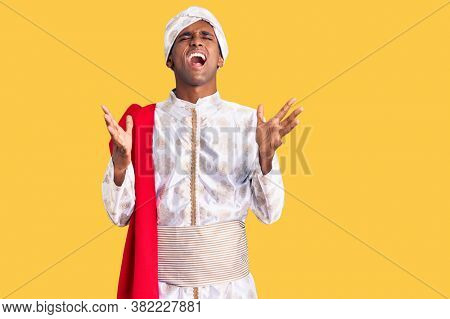African handsome man wearing tradition sherwani saree clothes celebrating mad and crazy for success with arms raised and closed eyes screaming excited. winner concept 