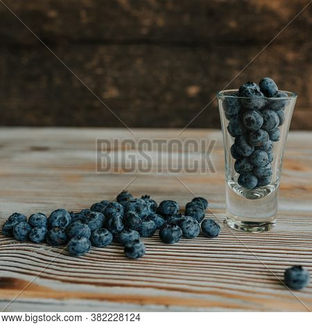 Fresh Blue Matte Round Blueberries Filled In A Transparent Glass And Scattered