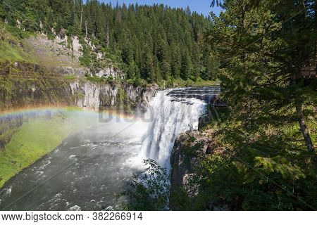 A Rainbow In The Mist Of Upper Mesa Falls As It Cascades Over A Cliff In The Rugged Wilderness Of He