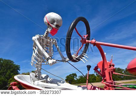 A Skeleton With A Covid-19 Mask Is Steering An Old Red Tractor.