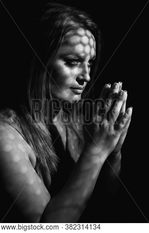 Beautiful woman confesses in the confessional, black and white. Praying woman, fine art portrait with interesting ligth and shadow pattern. Absolution. 