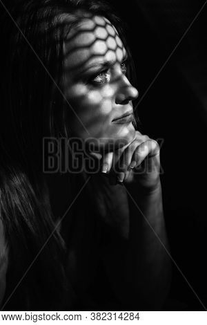 Beautiful woman confesses in the confessional, black and white. Praying woman, fine art portrait with interesting ligth and shadow pattern. Absolution. 