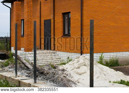 Cement Base For The Fence Against The Background Of A House Under Construction Made Of Red Facing Br