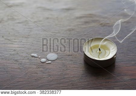 A Smoking Candle On A Wooden Table. A Darkened Small Candle Next To The Wax Camles On The Table. Cop