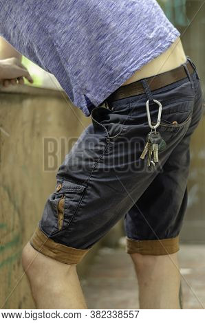 Young Man Stands In The Street With His Elbows On Stone Fence. Set Of Keys Hangs On The Belt. Lifest