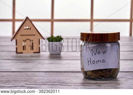 Savings For A New Home Concept. Glass Jar With Coins And Miniature House Moden On Wooden Table.