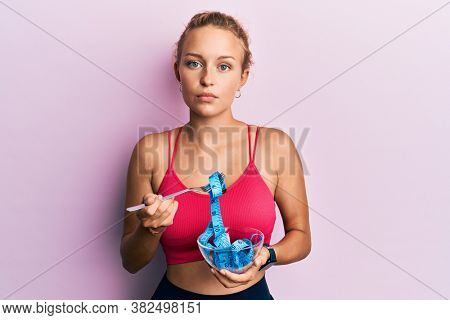 Beautiful caucasian woman eating measure meter doing diet for weight loss relaxed with serious expression on face. simple and natural looking at the camera. 