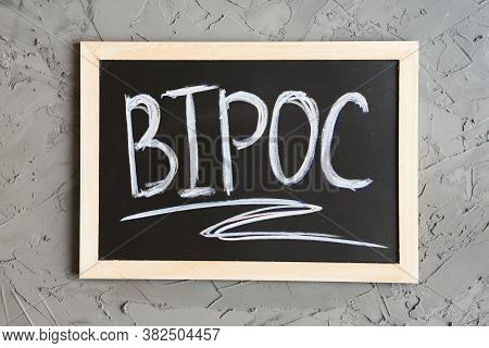 Bipoc Acronym Written On A Small Blackboard, Concrete Wall As Background. Bipoc Means Black, Indigen