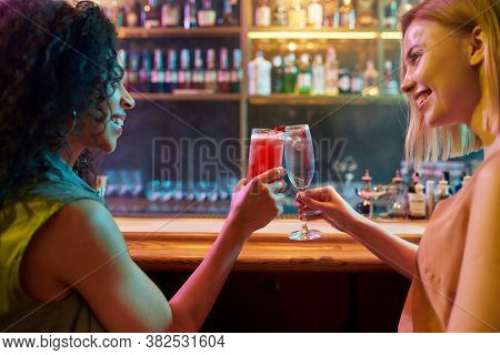 Weekend Time. Two Women Having Fun, Toasting, Drinking Cocktails While Sitting At The Bar Counter. F