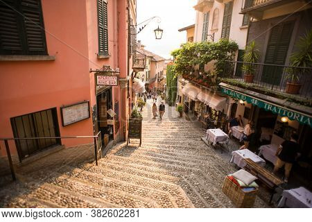 Bellagio. Lake Como. Italy - July 20, 2019: Amazing Old Narrow Street in Bellagio. Lake Como, Italy, Europe. Famous Picturesque Cobblestone Street with Souvenir Shops, Restaurants and Cafes.
