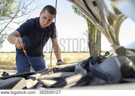 The Man Checks The Oil Level. Male Hands Hold A Dipstick, Which Shows The Level Of Engine Oil. Serio