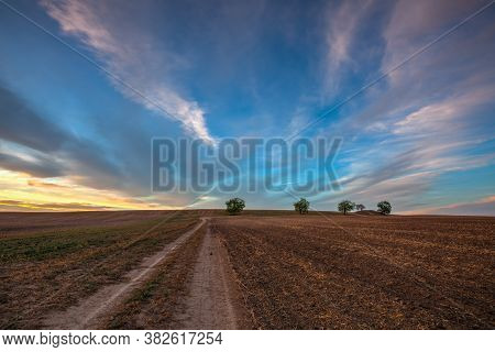 On The Dirt Road Between Empty Field After Harvesting In Summer Evening. Czech Republic. Amazing Sun