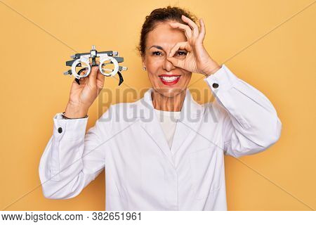 Middle age senior oculist woman holding optometrical glasses for vision correction with happy face smiling doing ok sign with hand on eye looking through fingers