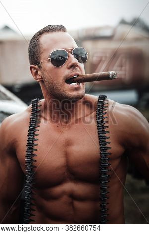 Muscular Man With Camouflage Shorts Relaxing With Airplane On The Background. Military Bodybuilder S