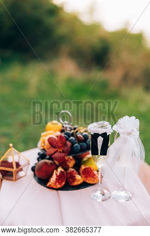 A Painted Table With A Bookcase With Fruits And Glasses For Champagne In The Suits Of The Bride And 