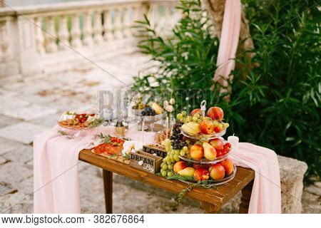 A Small Wooden Table With A Shelf Of Three Tiers With Fruits On A Table Set For The Celebration On A