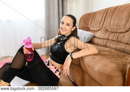 Fitness At Home. A Young Beautiful Woman In Sportswear With Headphones Sits Near Sofa In Cozy Homely